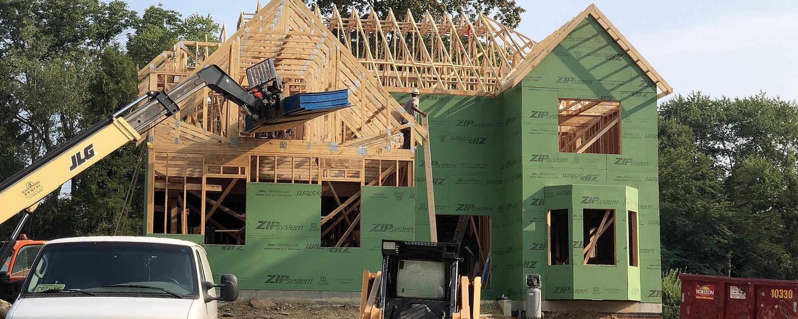 A wood-frame house half built, with a truck and loader parked in front