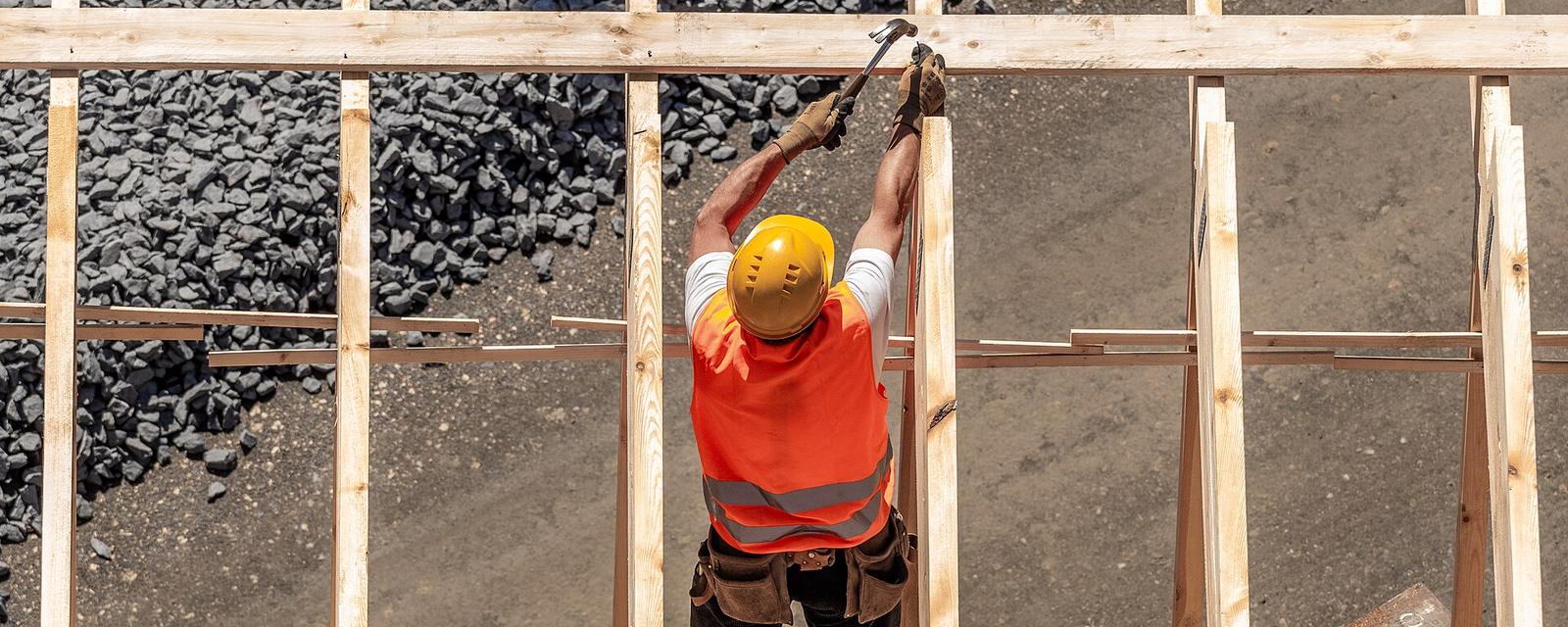 A carpenter in a hard hat nailing formwork on a construction site
