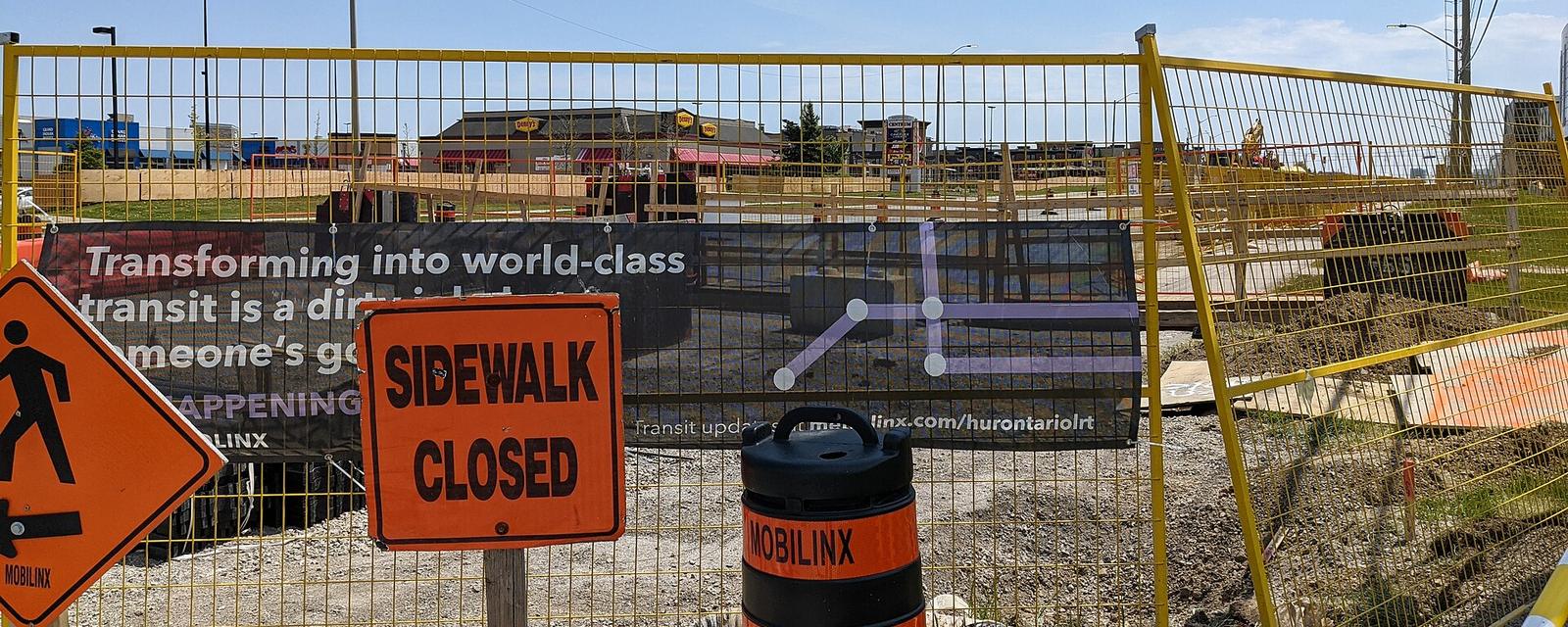 A fenced construction site with a sidewalk closed sign